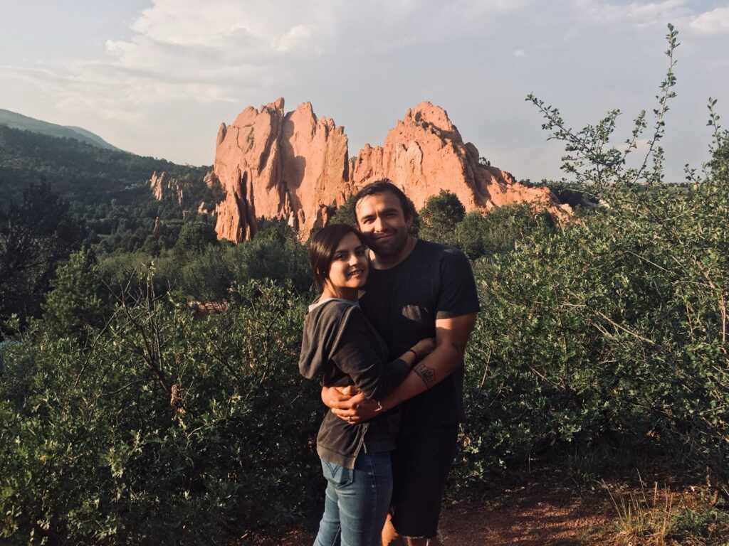 A couple holding each other standing in front of a rocky structure in the background.